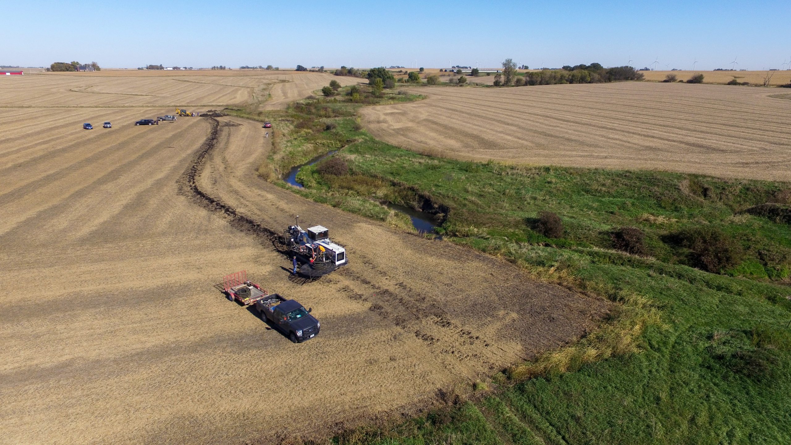 The view from an airplane of a drainage tile machine being used to install a saturated buffer distribution line in a harvested field along a stream in what is to become a saturated buffer.