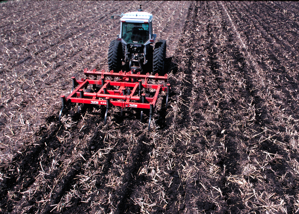A tractor pulling a plow leaving much of the crop residue from the previous crop on the soil surface.