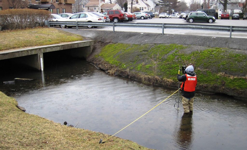 A hydrologist standing in a stream uses an instrument to measure stream discharge.