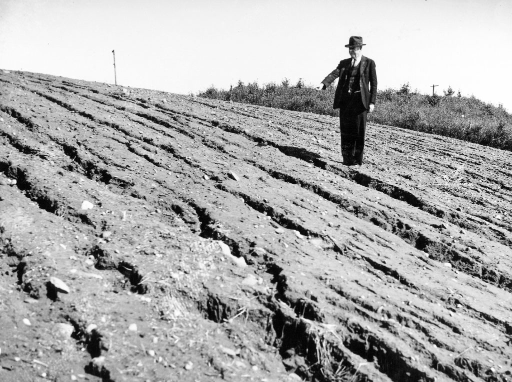 A mand stands on an eroded slope and pointing.