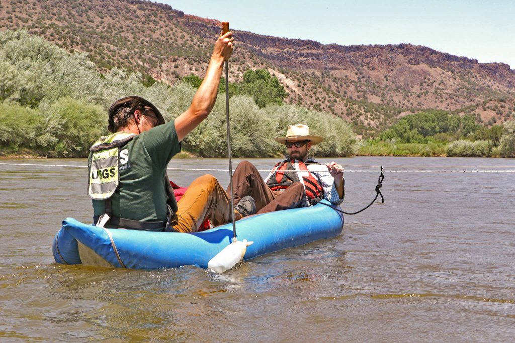 Two scientists collect river water samples from a boat