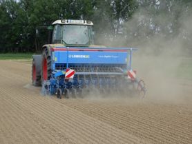 A tractor pulling a seed drill in a field.