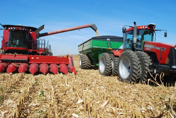 Un carro de grano unido a la parte trasera de un tractor en un campo. Una cosechadora está vaciando su tanque de retención en el carro de granos.