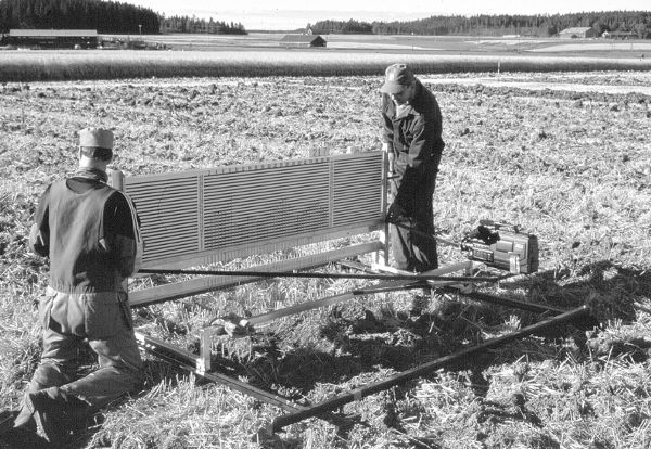 Two men on either side of a soil roughness meter using it in a field.