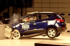 Auto azul ocupado por un maniquí de choque, mostrando señales de daños extremos luego de ser estrellado contra una barrera de concreto.
