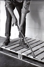 A waist-down picture of a man using a crowbar to pry up slats on a wooden pallet. 