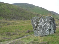 A large rock standing on a green hillside.