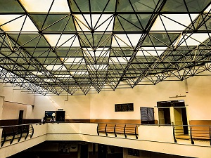An auditorium with a ceiling consisting of square tiles, each row supported by a network of metal trusses that form triangular prisms whose base is formed by the tiles.