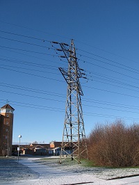 A metal power line tower in a snowy field.