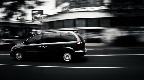 A black van moving quickly along a city road, with a blurred background.