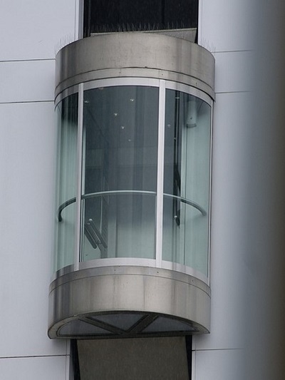 A glass-sided, hemicylindrical elevator in an exterior shaft.
