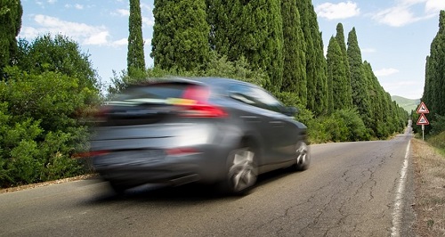A car, blurred by speed, moving quickly down a tree-lined road.