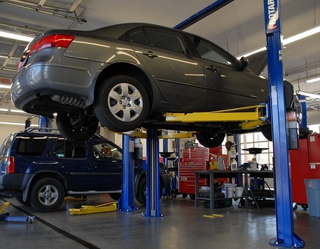 A car in a mechanic's shop is raised off the ground by a lift.