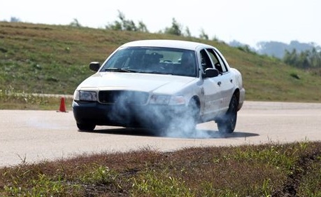 A white car braking heavily on a country road, with smoke coming from the tires.