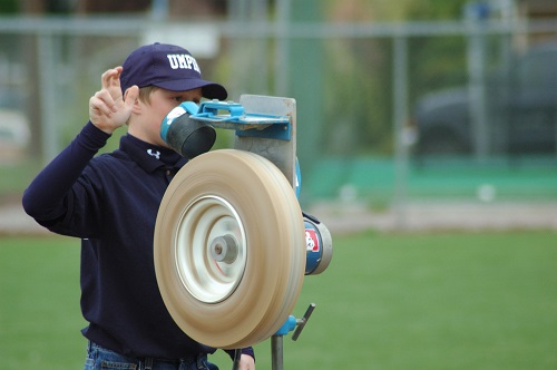 Un niño que opera una máquina lanzadora en un campo de béisbol.