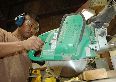A man is using a saw with a circular rotating edge to cut wood.