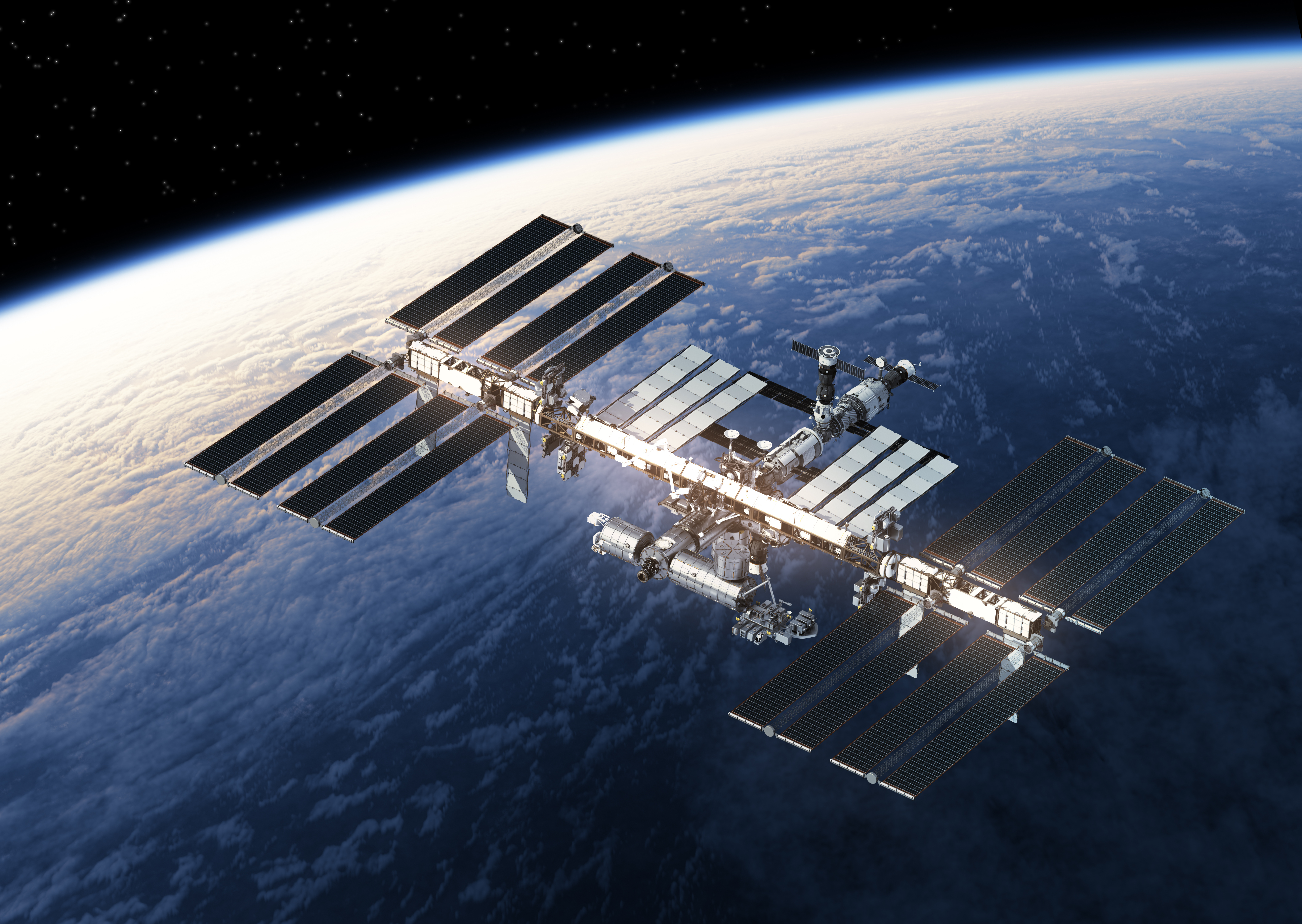 The International Space Station orbits above Earth, with its solar panels extended, against the backdrop of the planet&rsquo;s surface and the blackness of space.